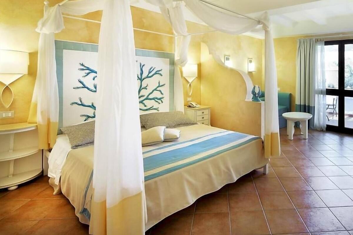 A bedroom with a canopy bed, a bedside table, a nightstand, and a view of the outdoors.