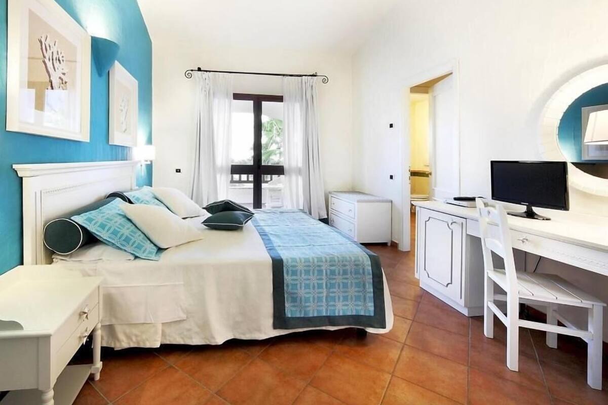 A bedroom with a bed, a desk, a chair, and a TV.