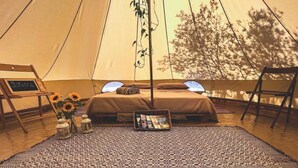 A tent interior with a patterned rug, a bed with pillows, a side table with a lantern, and a chair. - Pasare Glamping (Perfugas)