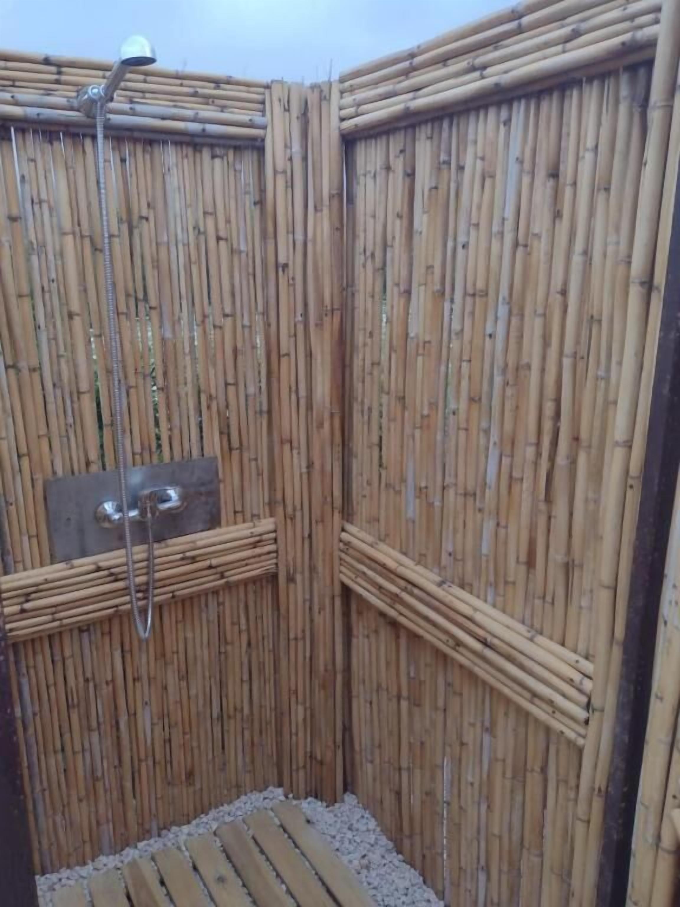 Compartimento de chuveiro em bambu, com chuveiro manual e torneira fixada na parede.