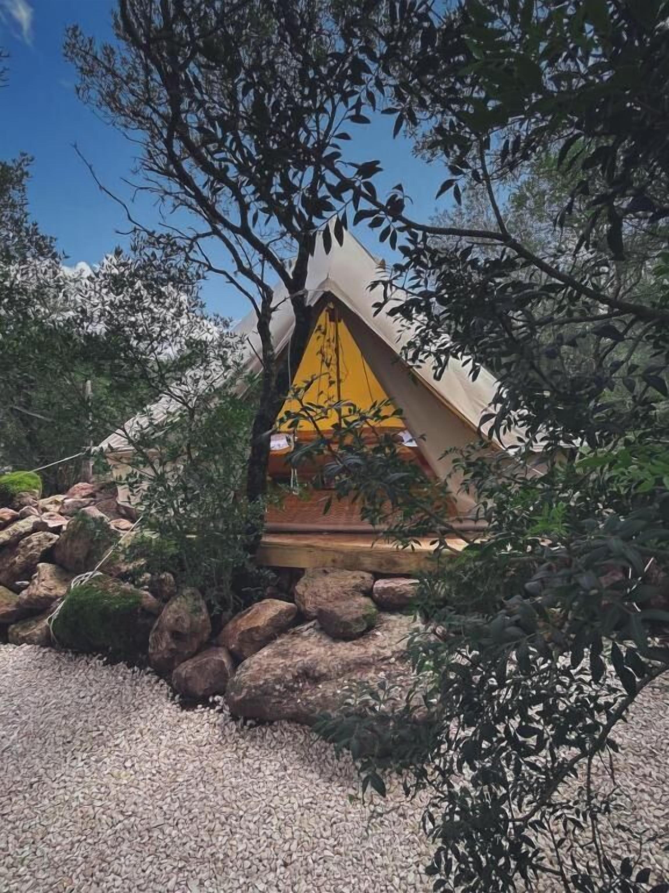 A triangular tent-like structure with a yellow interior, surrounded by rocks and trees.