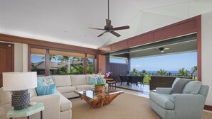 A spacious living area with a sofa, armchair, and coffee table, featuring a large window with a view of the ocean.