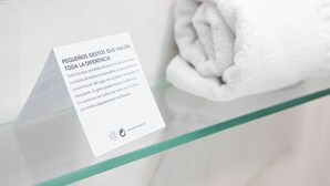 Une serviette blanche pliée est posée sur une étagère en verre, et un panneau en espagnol explique comment de petits gestes peuvent avoir un impact significatif.