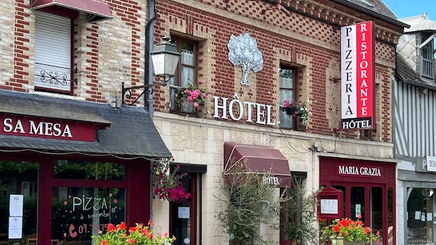 A hotel with a sign reading "HOTEL" and "PIZZERIA HOTEL" above the entrance. There are flower pots outside and a signboard with menu items. - Maria Grazia Hotel (Saint-Gatien-des-Bois)