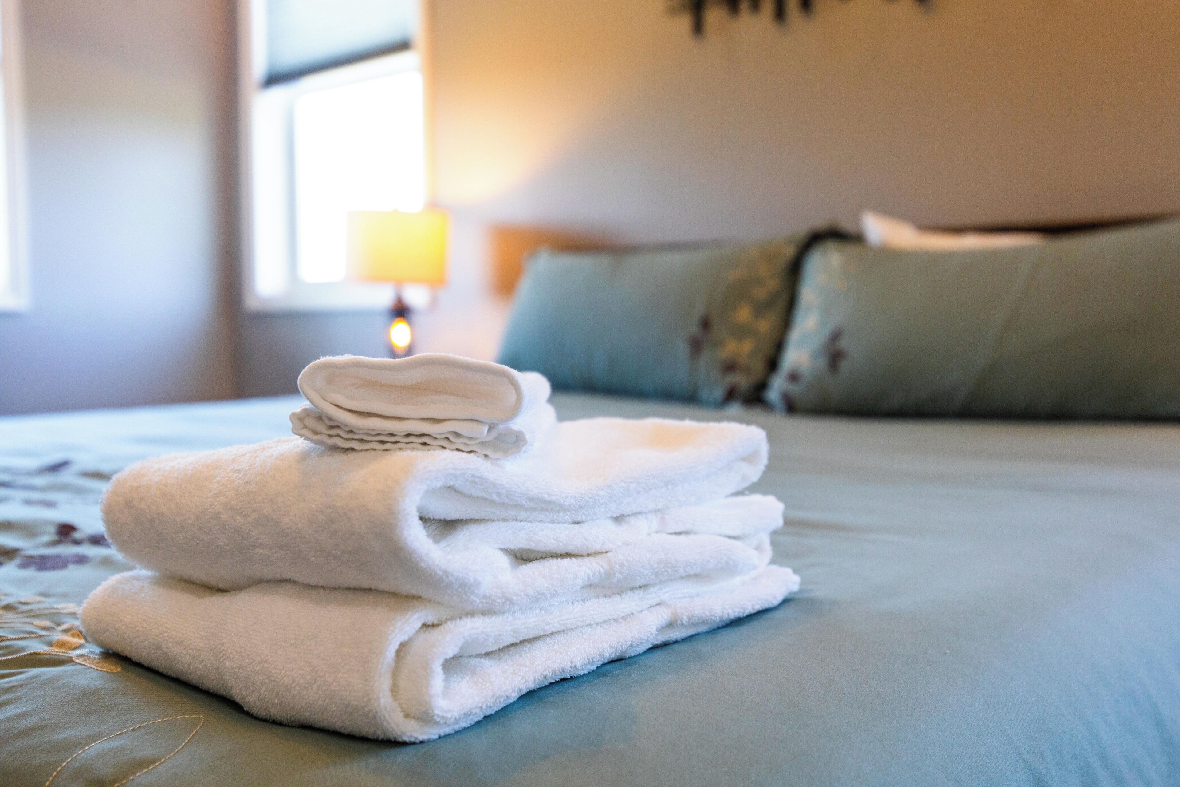 A neatly folded stack of white towels on a bed with a blue bedspread.