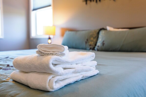 A neatly folded stack of white towels on a bed with a blue bedspread.