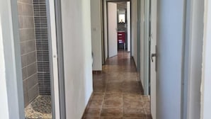 Un corridoio con pavimento piastrellato, pareti bianche e porte che conducono a diverse stanze.