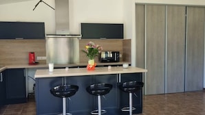 Una cucina moderna con isola centrale, tre sgabelli da bar, forno a incasso e televisore piatto.