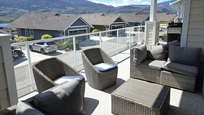 Een balkon met rieten meubilair, een barbecue en uitzicht op huizen en bergen.