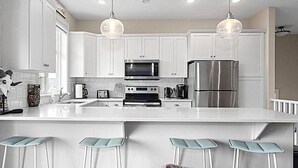 Een moderne keuken met witte kasten, roestvrijstalen apparatuur, een centraal kookeiland met barstoelen en hanglampen.