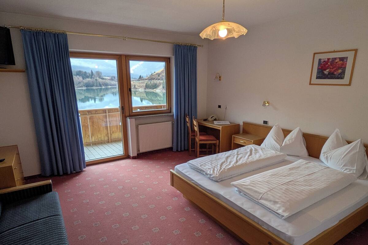 Une chambre d’hôtel équipée d’un lit, d’un bureau, d’une chaise et offrant une vue sur un lac grâce à de grandes fenêtres.