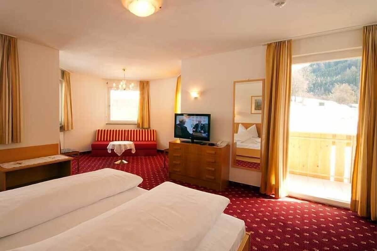 Une chambre d’hôtel avec deux lits, une télévision, une commode en bois, une fenêtre avec des rideaux et une vue sur un paysage enneigé.