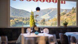 A dining area with a table set for two, a view of a lake and mountains through a window, and a small Christmas tree. - Hotel Seehof (Monguelfo)