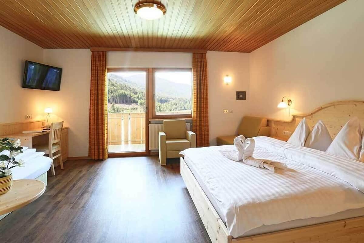 Une chambre d’hôtel avec un plafond en bois, un lit avec du linge de maison blanc, un bureau avec une lampe, une chaise et un téléviseur fixé au mur.