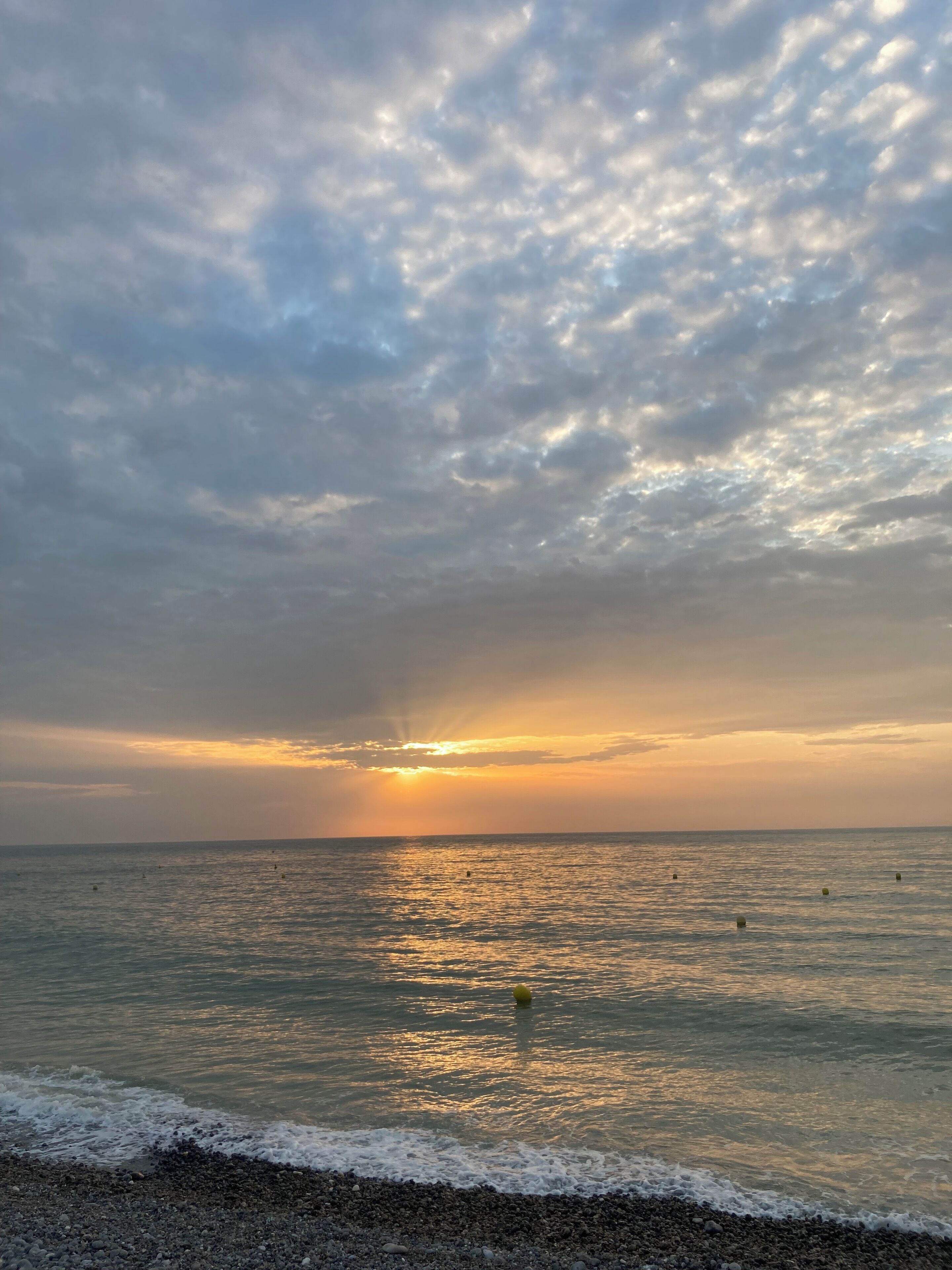 A beach with a sunset, calm sea, and a pebbly shore.