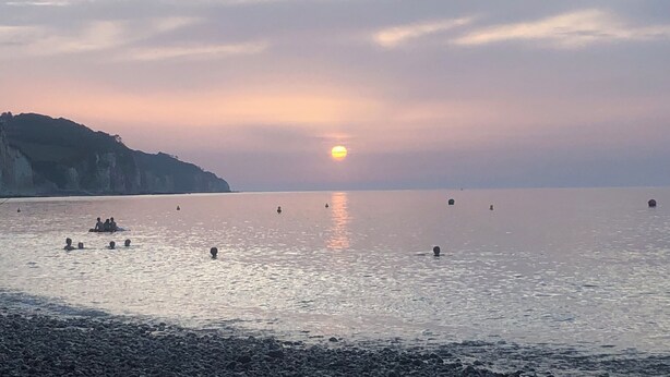 Mar serena a la posta de sol amb vaixells i un litoral rocos.