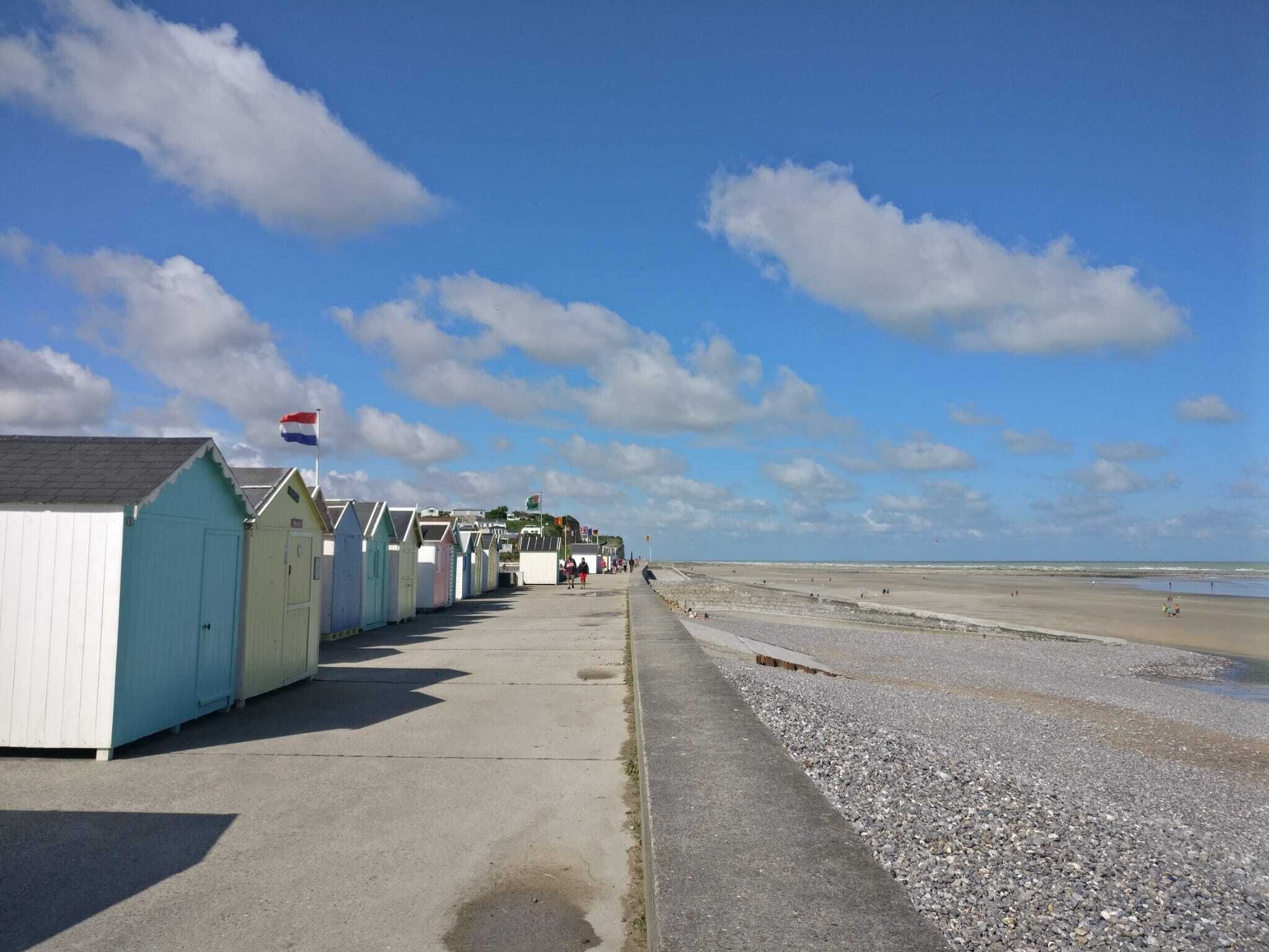 A row of beach huts along a pebbled beach with a clear sky.