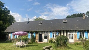 Una casa típica amb estructura de fusta i enduints, amb teulada inclinada, una xemeneia i un petit porxo amb taula i cadires.