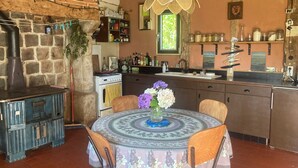 Una cuina rústica amb paret de pedra, una estufa antiga i una taula de dinar de fusta amb cadires.