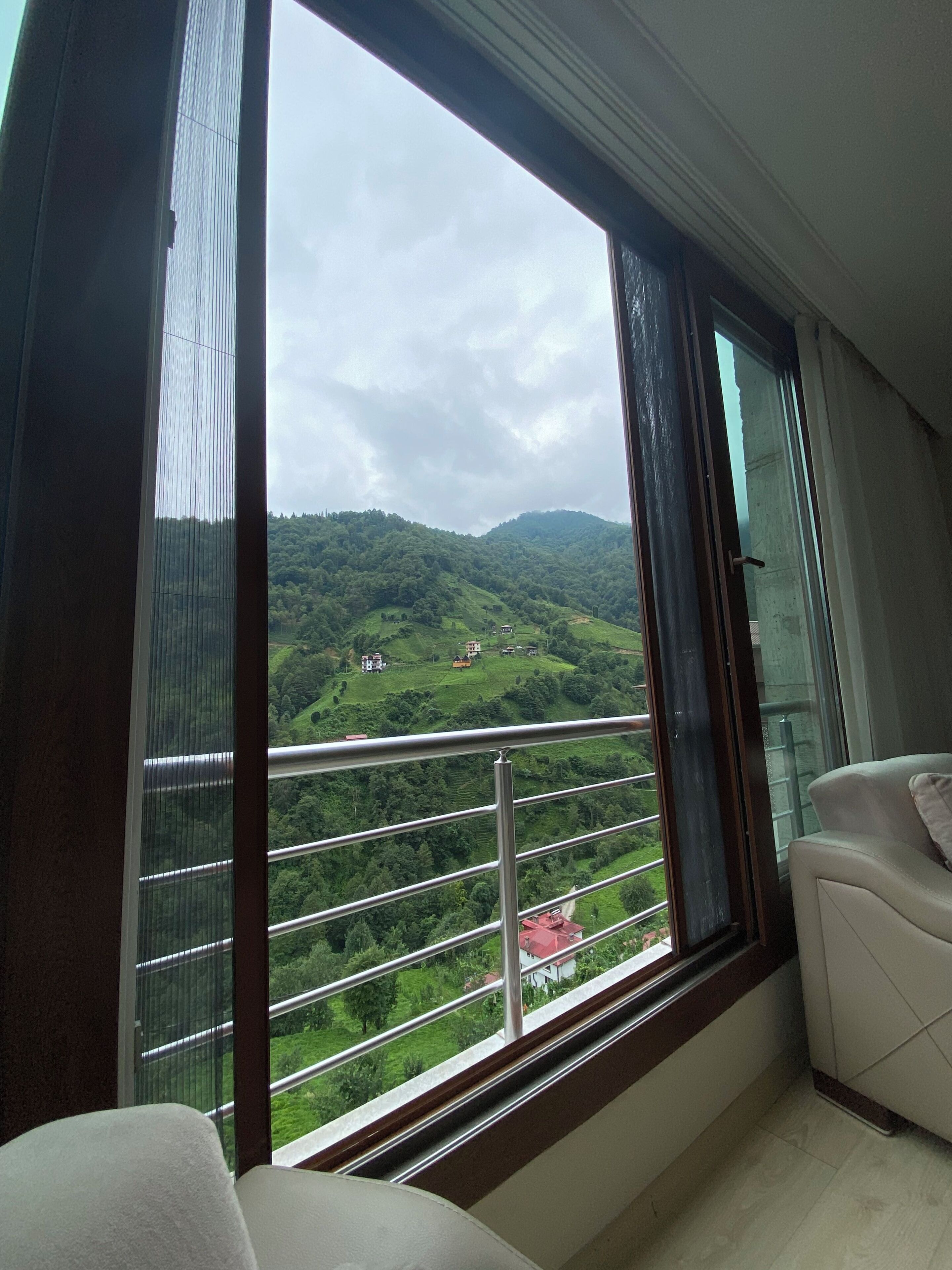 A room with a large window overlooking a green landscape with hills and a few buildings.