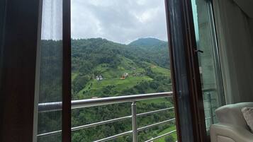 Ein Zimmer mit großem Fenster und Blick auf eine grüne Landschaft mit Hügeln und einigen Gebäuden.