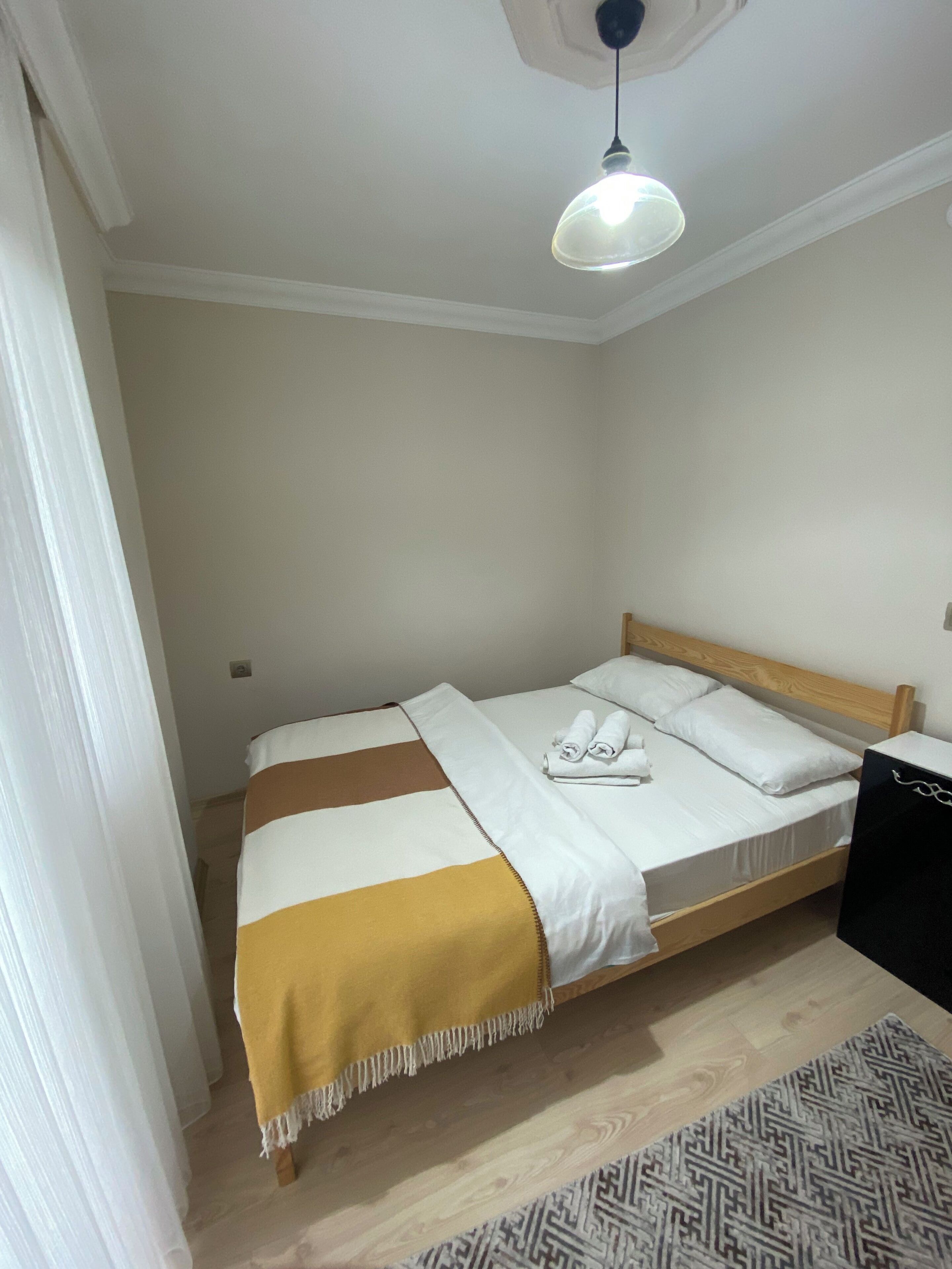 A single bed with a wooden headboard, a white and brown striped blanket, and two rolled towels on the bed.