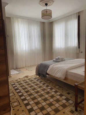 A bedroom with a bed, a patterned rug, and sheer curtains.