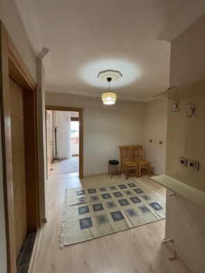 A hallway with a patterned rug, wooden chairs, a ceiling light fixture, and a door leading to another room. - Green House 1934 (Çamlıhemşin)