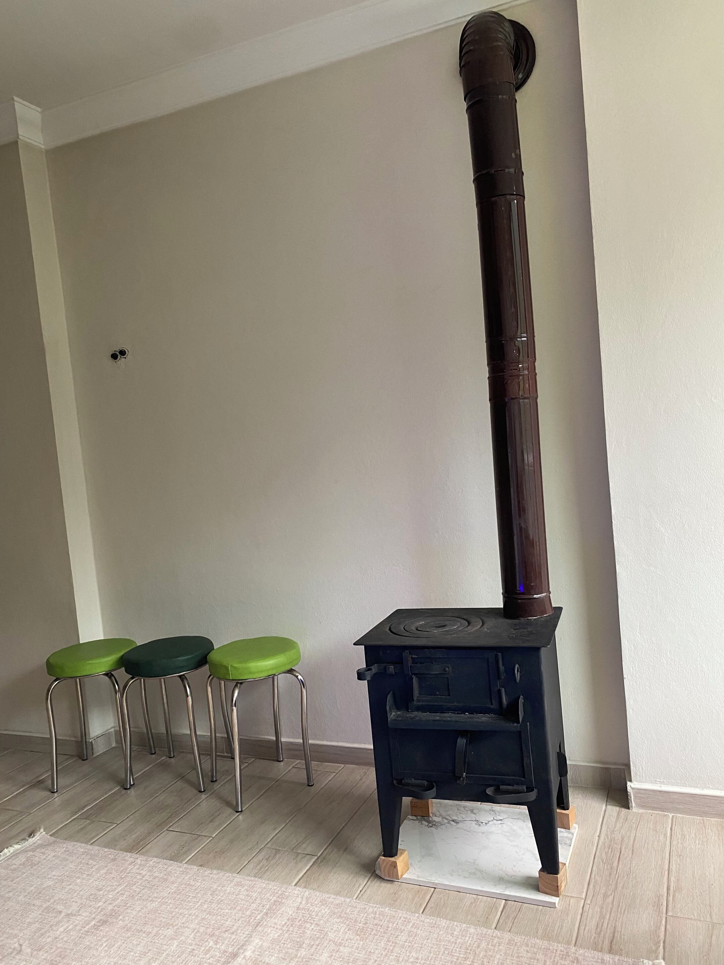 A room with a wood-burning stove, three green stools, and a white floor.