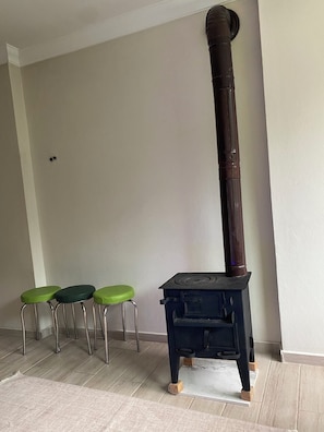 A room with a wood-burning stove, three green stools, and a white floor.