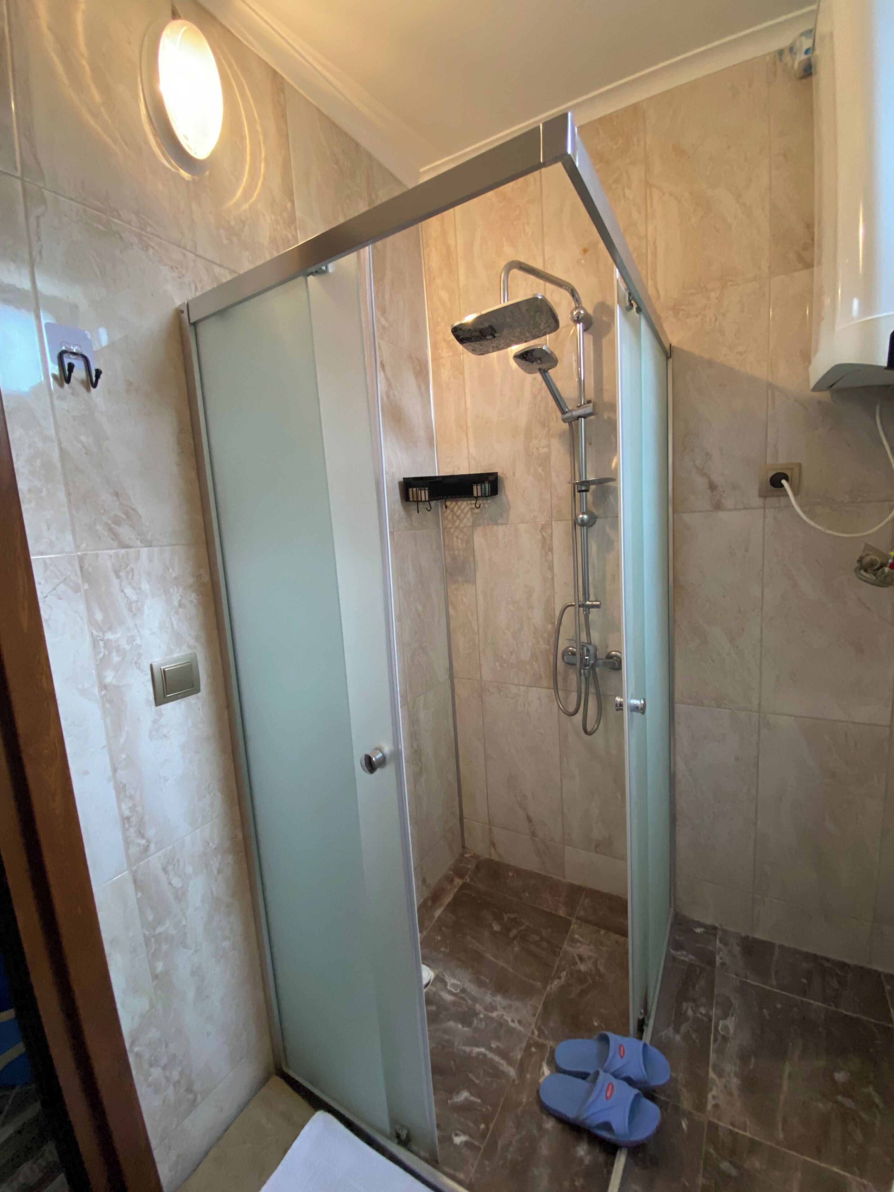 A walk-in shower with a glass door, a handheld showerhead, and a handheld shower head.