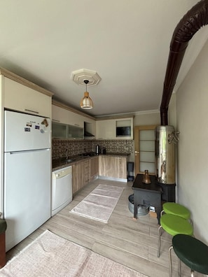 Una cocina compacta con refrigerador, estufa, pileta y un pequeño comedor con taburetes.