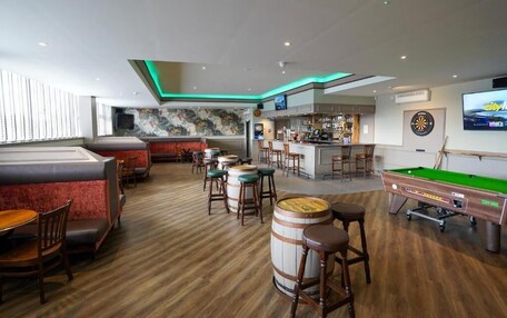 A bar area with wooden flooring, stools, a pool table, and a dartboard.