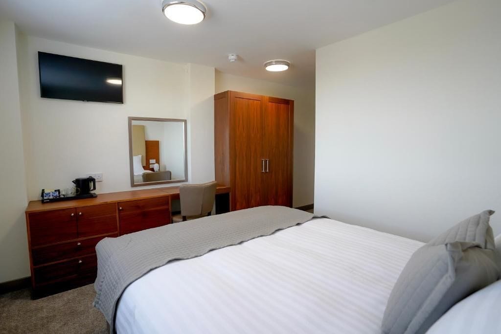 Habitación de hotel con cama, armario de madera, escritorio con silla, televisor de pantalla plana y espejo.