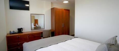 Habitación de hotel con cama, armario de madera, escritorio con silla, televisor de pantalla plana y espejo.