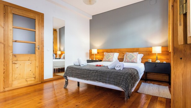 A bedroom with a wooden bed, two bedside tables with lamps, a wooden wardrobe, and a wooden floor. - Bairro Alto Two Bedroom Apartment (Lisbon)