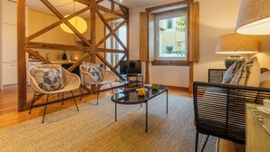A modern living room with a wooden ceiling structure, a glass coffee table, and two wicker chairs. - Bairro Alto Two Bedroom Apartment (Lisbon)