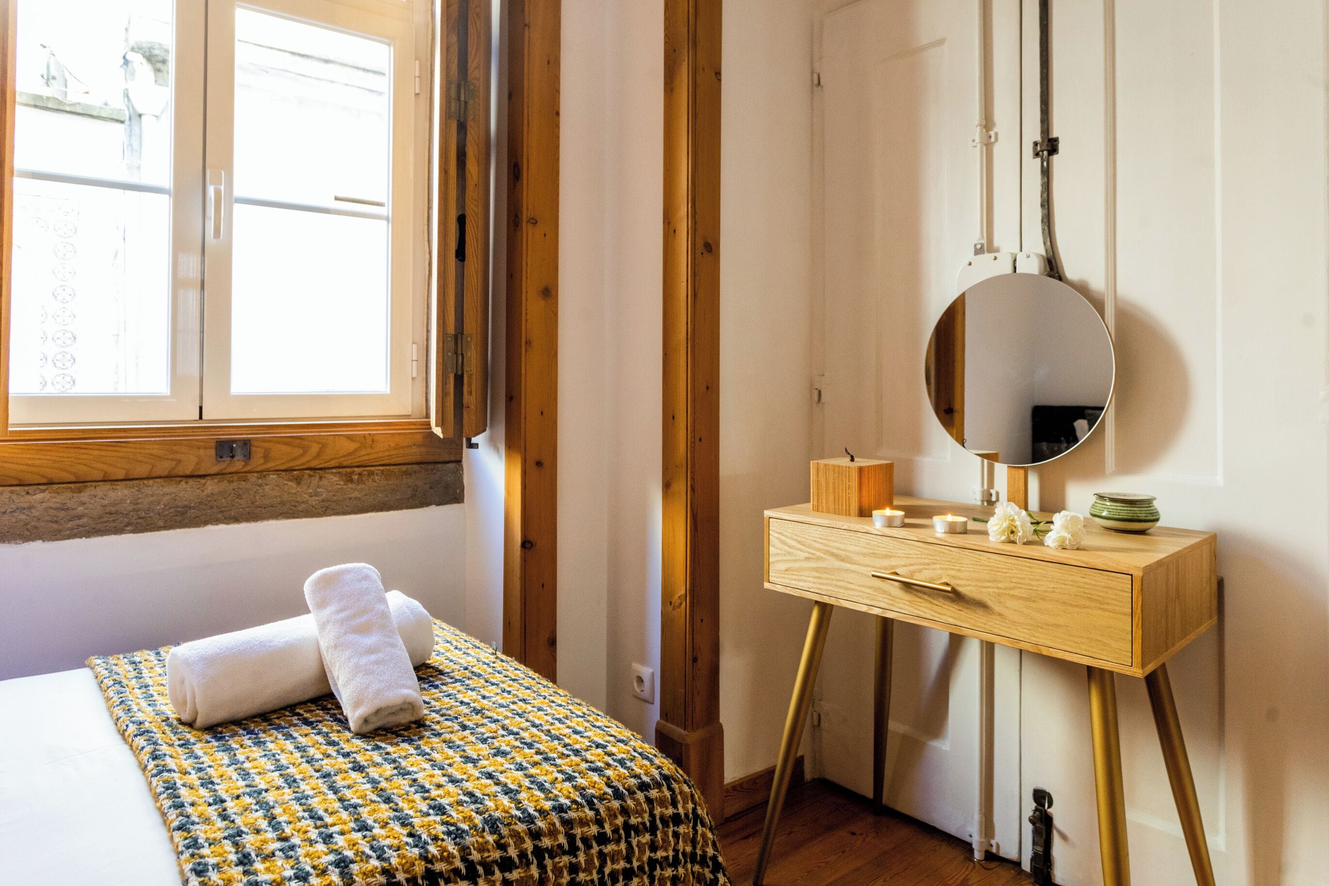 A bedroom with a bed, a wooden dresser, a mirror, and a window.
