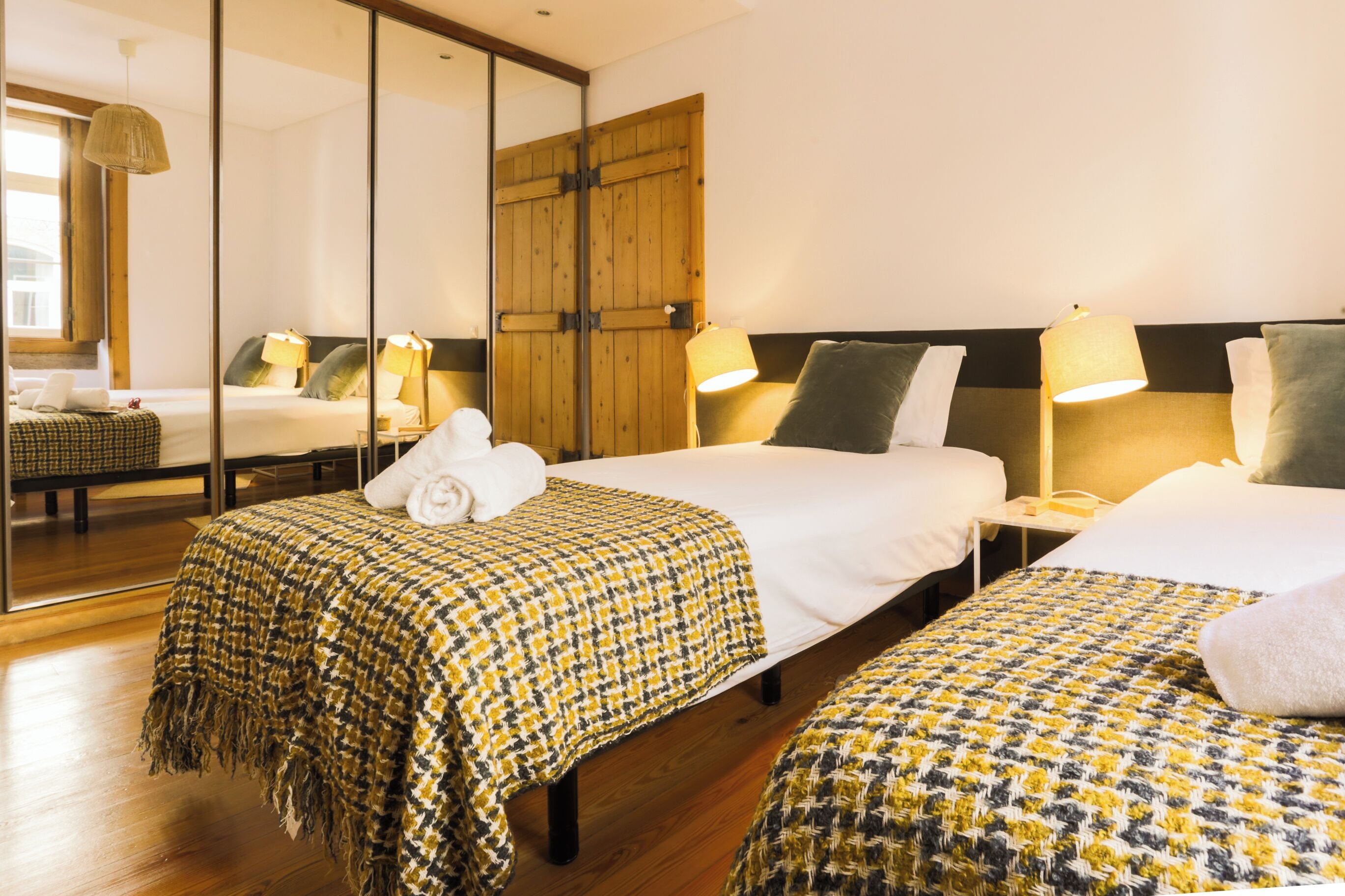 Habitación de hotel con dos camas, suelo de madera, un espejo grande y un armario de madera.