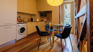 A compact kitchen with a washing machine, a dining table with chairs, and a hanging paper lantern. - Bairro Alto Two Bedroom Apartment (Lisbon)