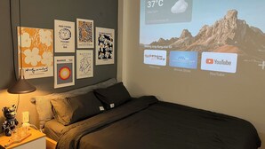 A bedroom with a bed, a nightstand, and a wall with art prints. - FlexiHome (Ho Chi Minh City)
