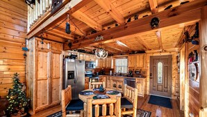 L’intérieur d’une cabane en rondins, avec une table à manger en bois, des chaises, un réfrigérateur, une cuisinière et un sapin de Noël.