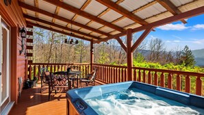 Une terrasse en bois avec un jacuzzi, du mobilier d’extérieur et une vue sur la forêt environnante.