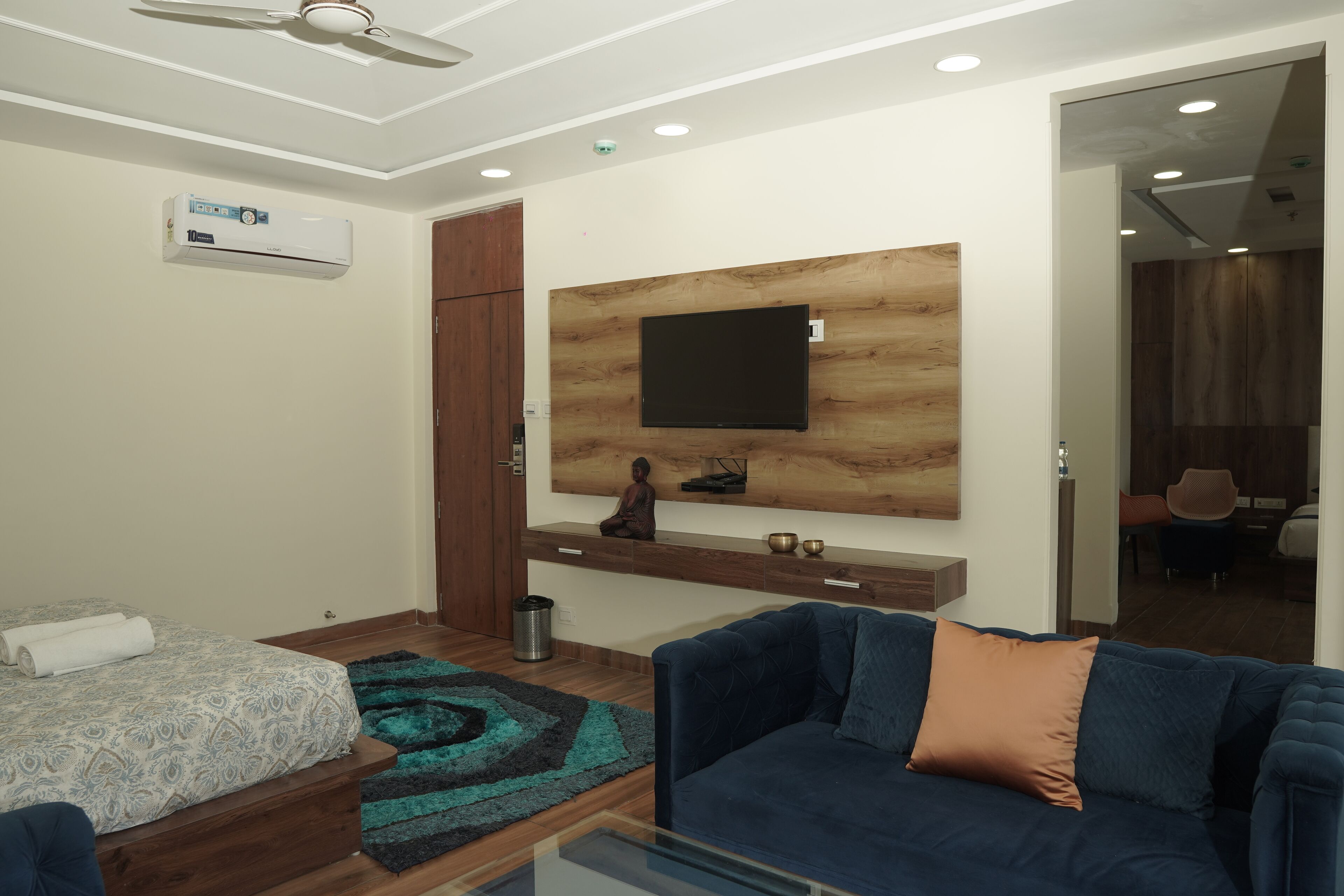 Une chambre d’hôtel moderne avec un lit, un canapé bleu, un téléviseur fixé au mur et un mur décoratif en bois.