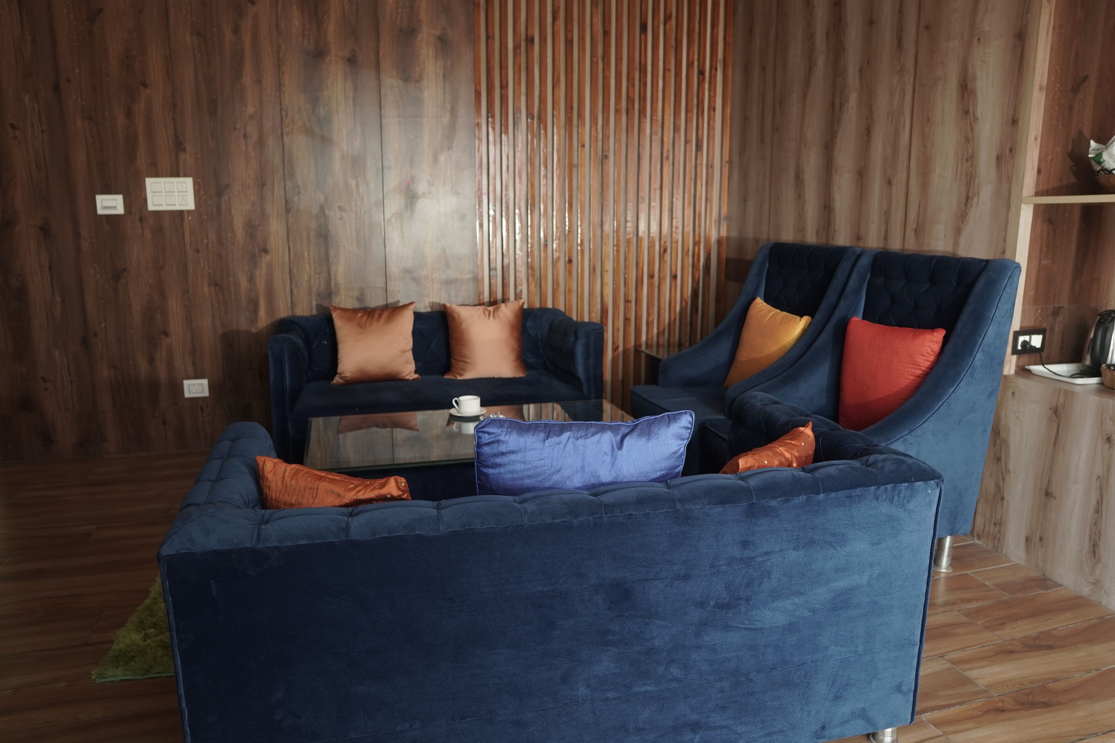 Un salón moderno con una mesa de centro de vidrio, dos sofás con cojines de colores y una pared de madera.