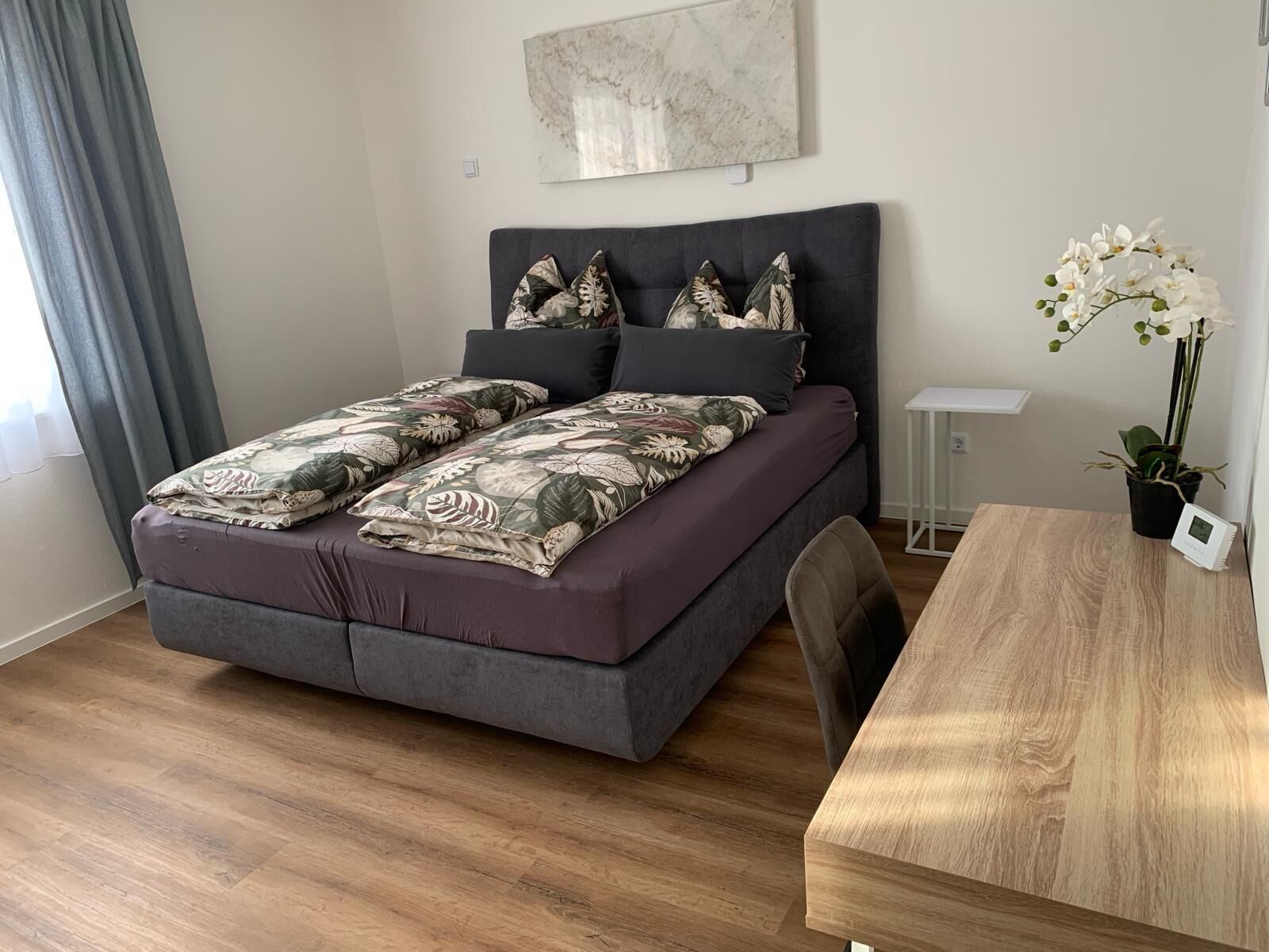 Une chambre à coucher moderne avec un grand lit, une table de chevet, une petite armoire blanche et une plante orchidée en pot.