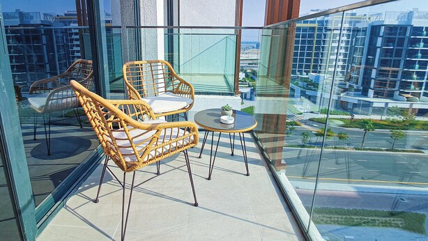 A balcony with wicker chairs and a small table, overlooking a cityscape with modern buildings. - Bloomfields Cozy STU in Azizi Riviera (Dubai)