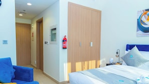 A hotel room with a bed, a blue sofa, a wardrobe, and a fire extinguisher. - Bloomfields Cozy STU in Azizi Riviera (Dubai)