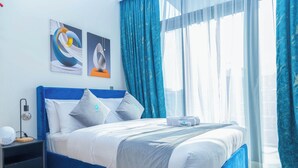 A modern bedroom with a blue headboard, white bedding, and a bedside table with a lamp. - Bloomfields Cozy STU in Azizi Riviera (Dubai)