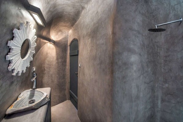 A modern bathroom with a unique curved wall design, a large mirror, a freestanding sink, and a shower.